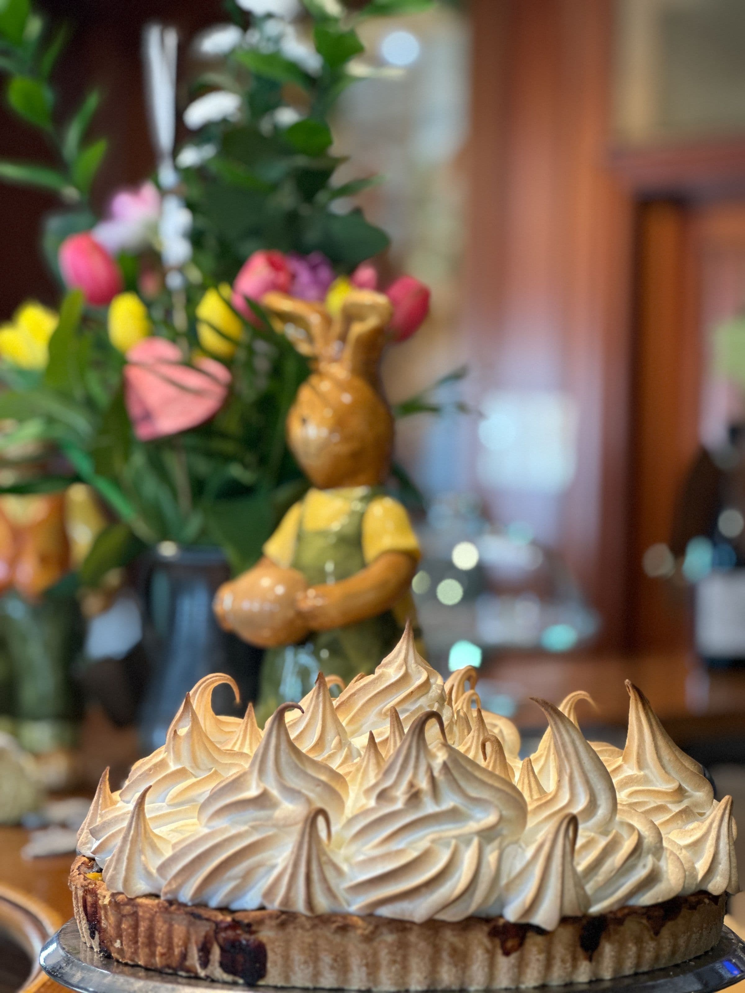Tarte meringuée fraîchement caramélisée en gros plan, posée devant des fleurs et une figurine en céramique, évoquant l’ambiance chaleureuse et artisanale du restaurant.