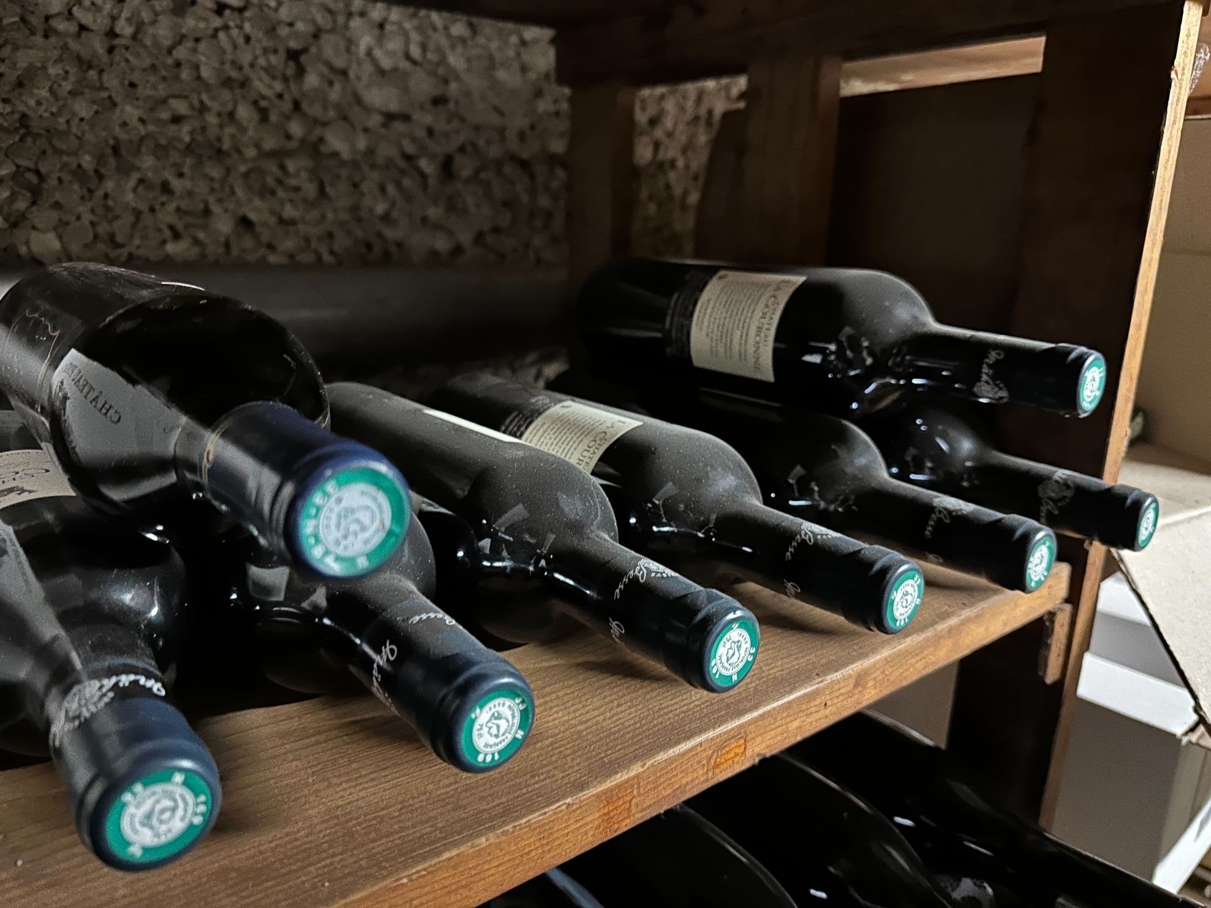 Gros plan sur des bouteilles de vin alignées à l’horizontale sur une étagère en bois, présentant une cave à vin poussiéreuse et traditionnelle.